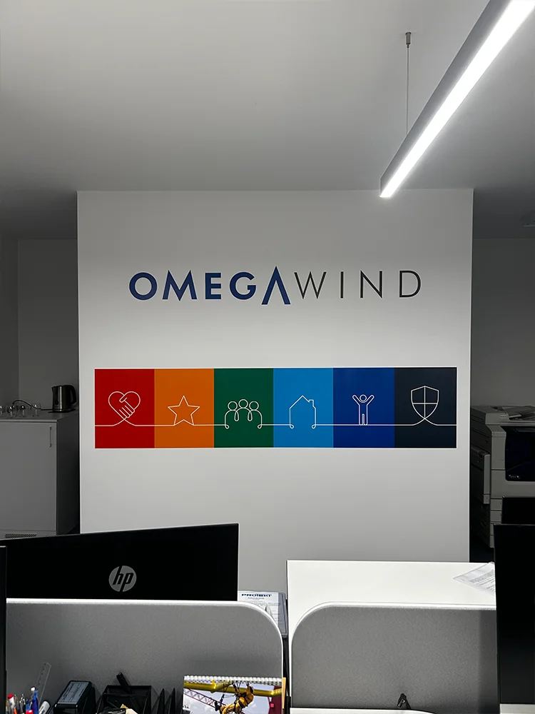 Logo OMEGAWIND nad kolorowym pasem ikon na ścianie biura