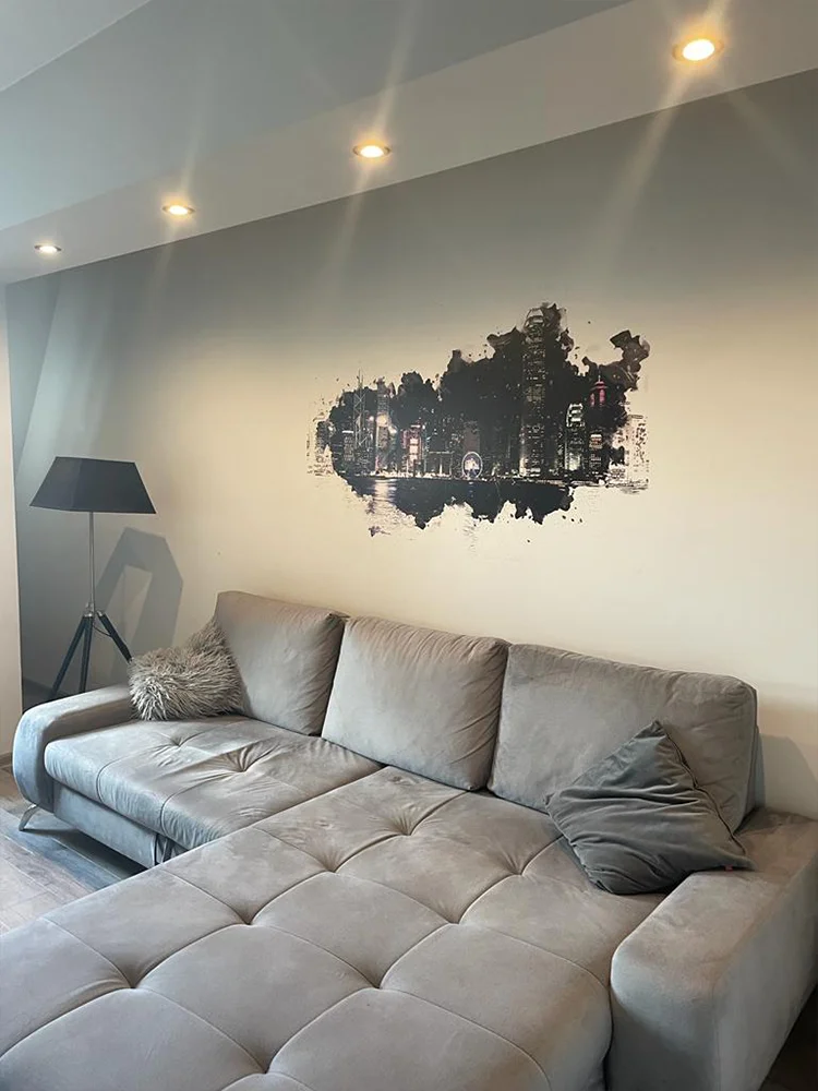 Panorama miasta wydrukowana na ścianie nad szarą sofą